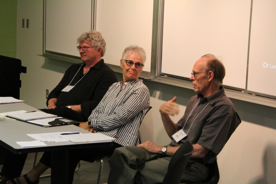 A woman and two men sit in discussion at the front of a classroom