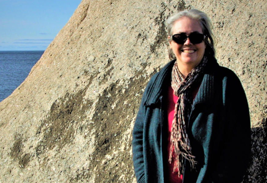 A smiling woman standing on a rocky beach