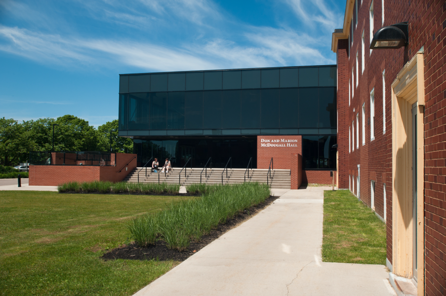 A building of brick and dark glass with green grass in the foreground and a blue sky behind