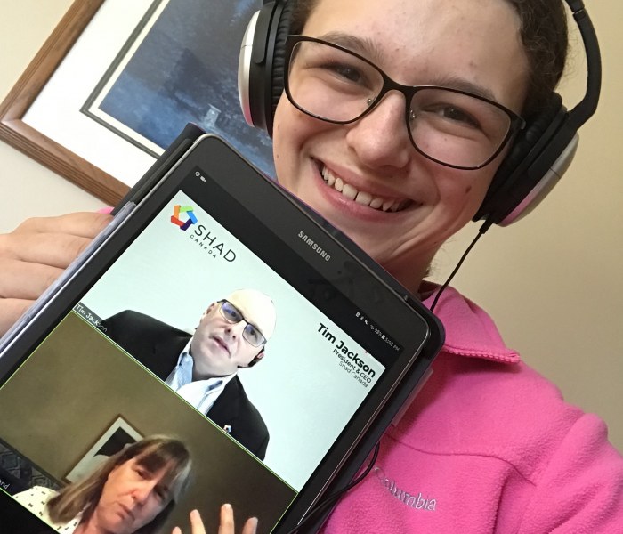 A young female holds up a digital tablet with the faces of a man and a woman on it