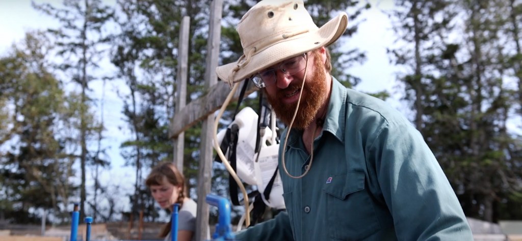 A beareded man in a floppy hat works on a farm