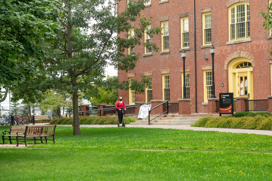 Photo of student riding scooter in front of SDU Main Building on the UPEI campus