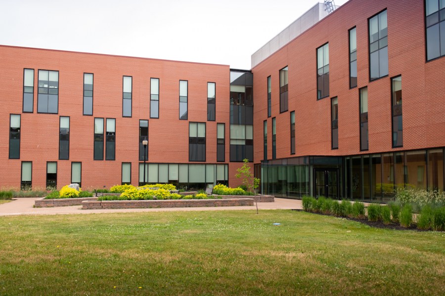 A modern-looking red brick building, three stories with two prominent wings. A landscaped garden with sitting space on benches in the foreground. 