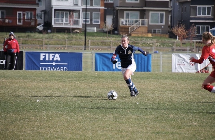 photo of woman dribbling soccer ball on a grass pitch