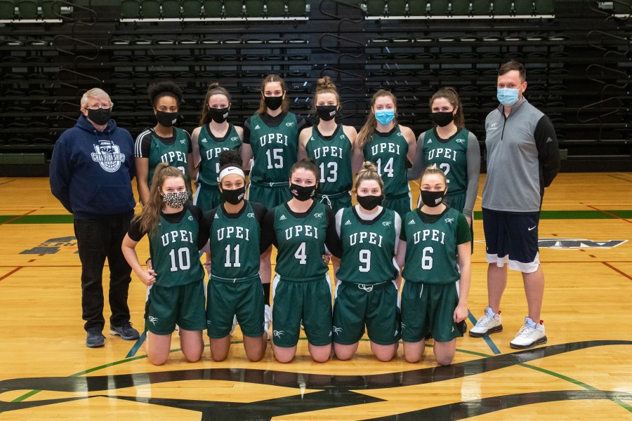 Photo of women's basketball team standing with coaches in the gym