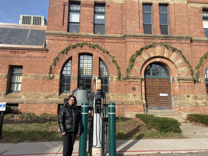 UPEI Environmental Studies student Ajhma Dhakal stands outside Charlottetown City Hall next to one of the city’s Electric Vehicle (EV) chargers