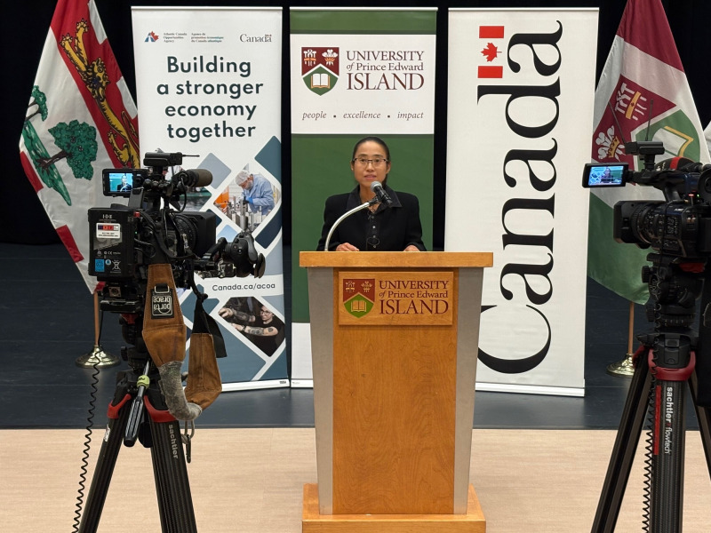 Photo of a woman standing at a podium flanked by video cameras