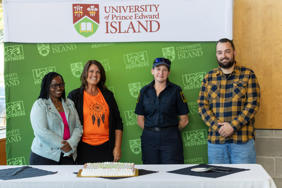 photo of four people standing behind a table with a cake and documents on it