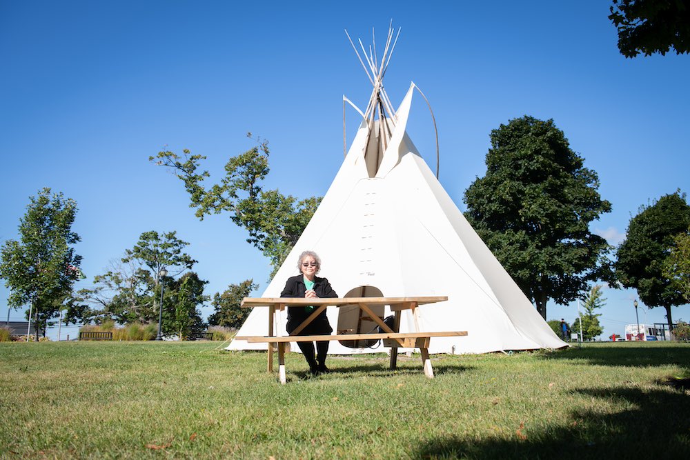 Dr. Angelina Weenie seated on a bench by the tipi in UPEI's quad