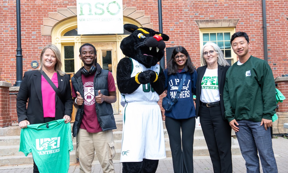 Diya Bubna, Pride the Panther, and others in front of UPEI's SDU Main Building