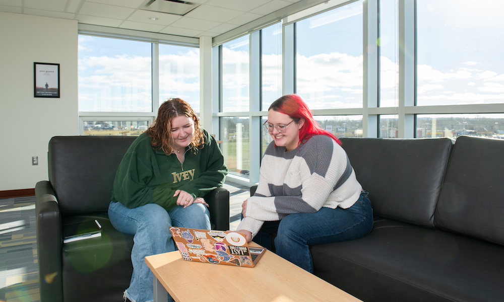 two UPEI students and a laptop computer in the Performing Arts Centre and Residence lounge