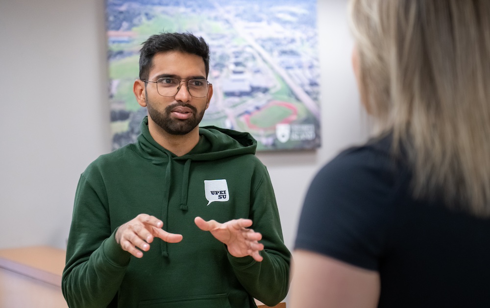 a UPEI student in a green UPEISU hoodie talking to a colleague