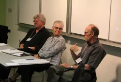 A woman and two men sit in discussion at the front of a classroom