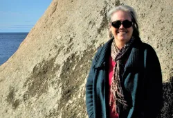 A smiling woman standing on a rocky beach