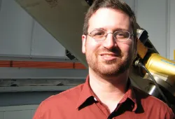 A smiling man in front of a telescope