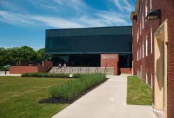 A building of brick and dark glass with green grass in the foreground and a blue sky behind