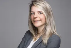 A portrait of a smiling young woman with long hair and a grey suit