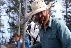 A beareded man in a floppy hat works on a farm