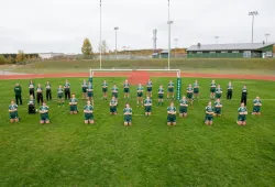 A group of female ruby players stand on a grass sports field