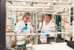 Two females in lab coats and protective goggles work in a chemistry lab filled with test tubes and chemical