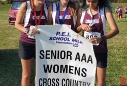 Three young females wearing matching running gear from Colonel Gray High School stand smiling with medals around their necks, holding a banner reading: SENIOR AAA WOMEN'S CROSS COUNTRY CHAMPIONS