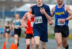 A young man running in a road race looking strong and confident with other runners trailing him