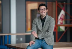 A smiling spectacled man in a casual blazer and jeans