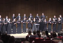 A small chamber choir on stage wearing black concert robes