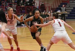 A femal baksetball player in green Panthers gear charges towards the basket in a game