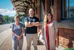 Barbara Rousseau, Dr. Josh MacFadyen, and Natalie Munn stand next to the former Charlottetown Railway station.