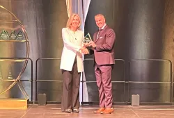 Woman handing a trophy to a man, standing on a stage