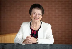 Photo of woman smiling leaning against railing with hands clasped