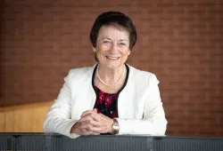 Photo of a smiling woman with hands folded leaning on a railing