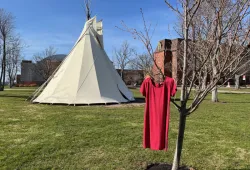 photo of a red dress hanging on a tree in front of a tipi