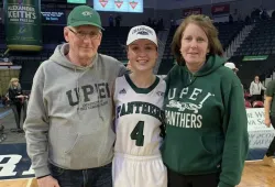 photo of man and woman standing on either side of basketball player, all wearing UPEI branded clothing