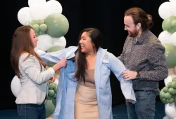 Giselle Kan, Class of 2028, receives her blue coat from her partner, Austin Gautreau, and her mentor and AVC alumna Dr. Lauren Brooks. 