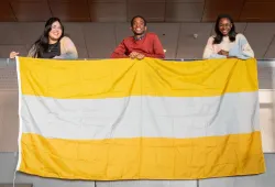 Photo of three people holding gold, silver, and bronze striped flag