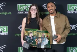 Photo of woman and man holding trophies in front of a backdrop