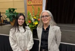 Photo of two women smiling standing in front of a stage and podium