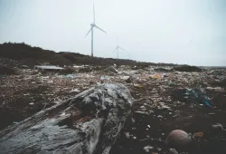 a garbage-covered shoreline with wind turbines in the background