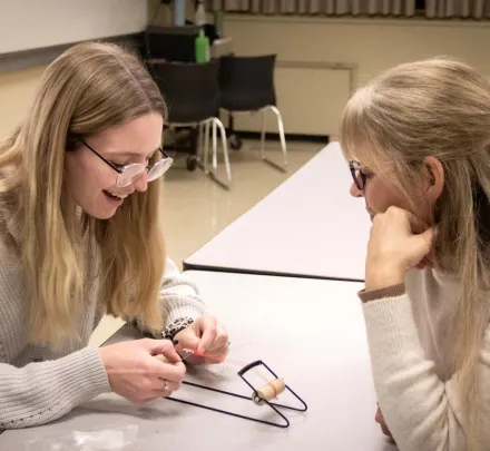 two people in a classroom using a small loom