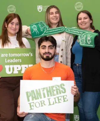 four UPEI students in front of a green backdrop with white and green balloons 