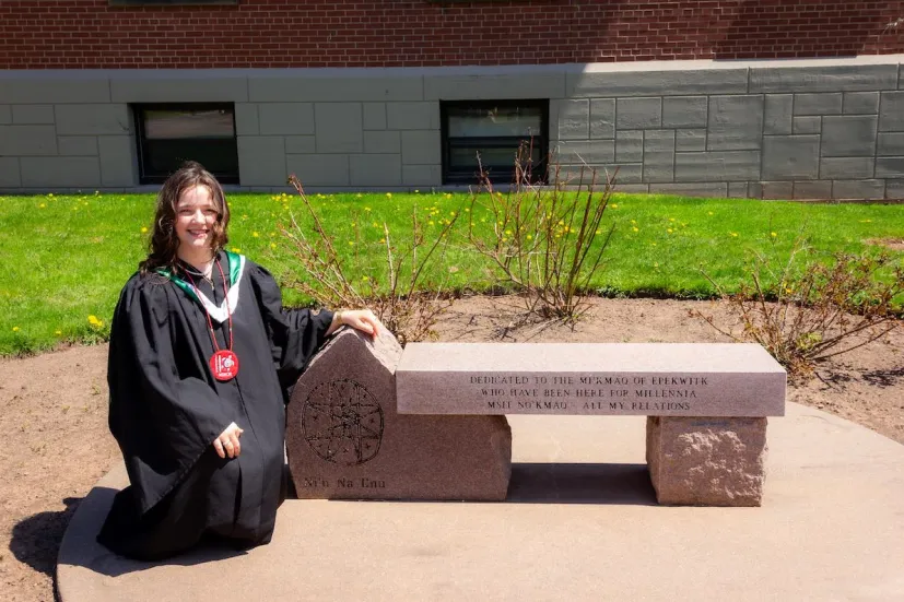 a UPEI graduate kneeling by a commemorative stone bench