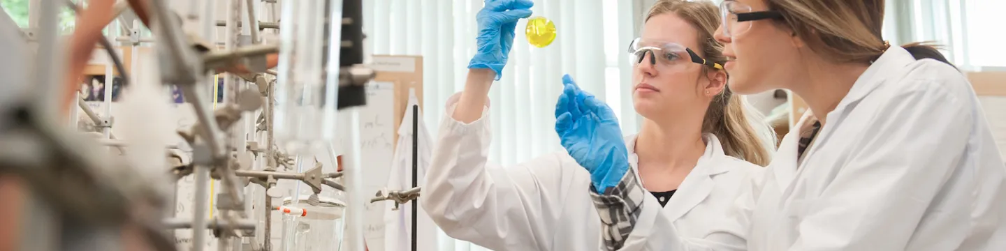 Student researchers examine a volumetric flask in a chemistry lab