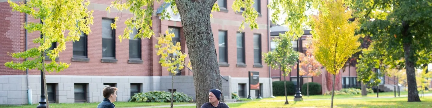 two students sitting in the UPEI quad with a large brick building in the background