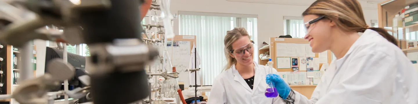 two chemistry students in laboratory with coloured flasks 