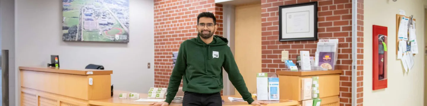 a UPEI student in a green UPEISU hoodie standing in an office