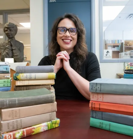 dr. kate scarth sitting in front of the lucy maud montgomery institute office door with stacked books in foreground