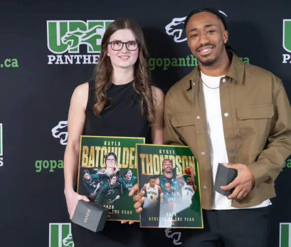 Photo of woman and man holding trophies in front of a backdrop